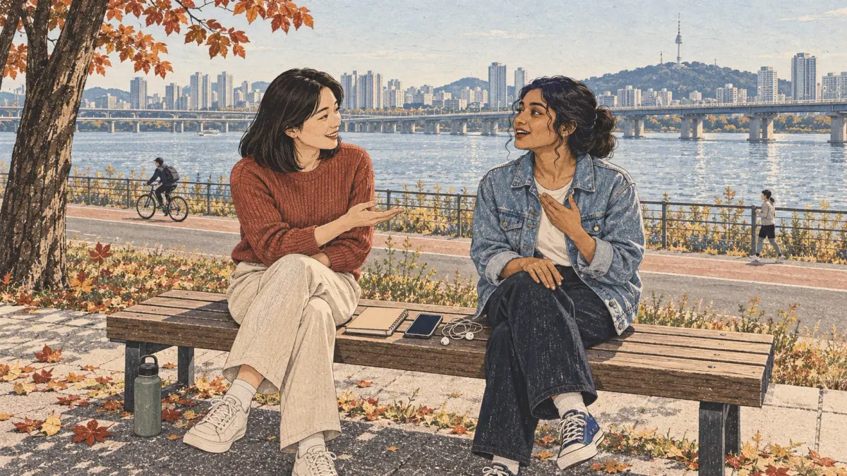 Two adult friends practise Korean together on a riverside bench in Seoul.